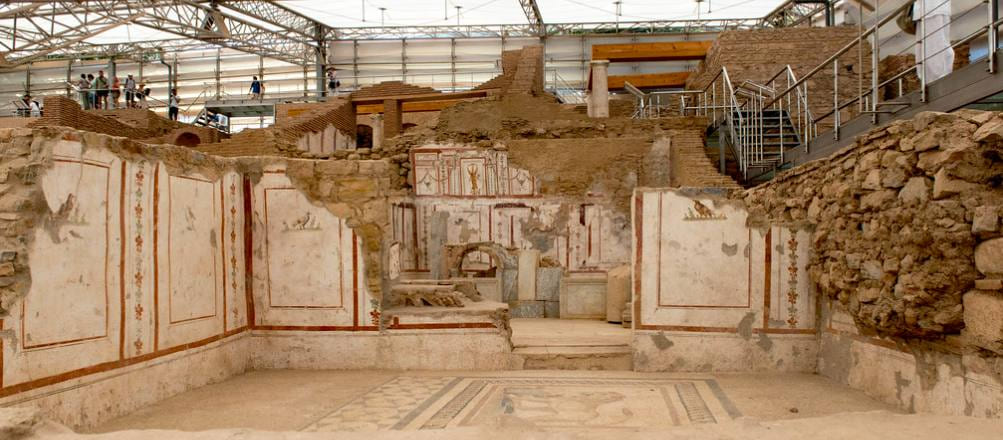 Sala excavada de las Casas Adosadas de Éfeso con paredes pintadas y suelo de mosaico geométrico bajo la cubierta moderna