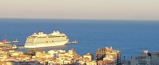 Un crucero atracado en el muelle de Kuşadası visto desde lo alto de la ciudad, con los tejados del centro en primer plano y el Egeo detrás