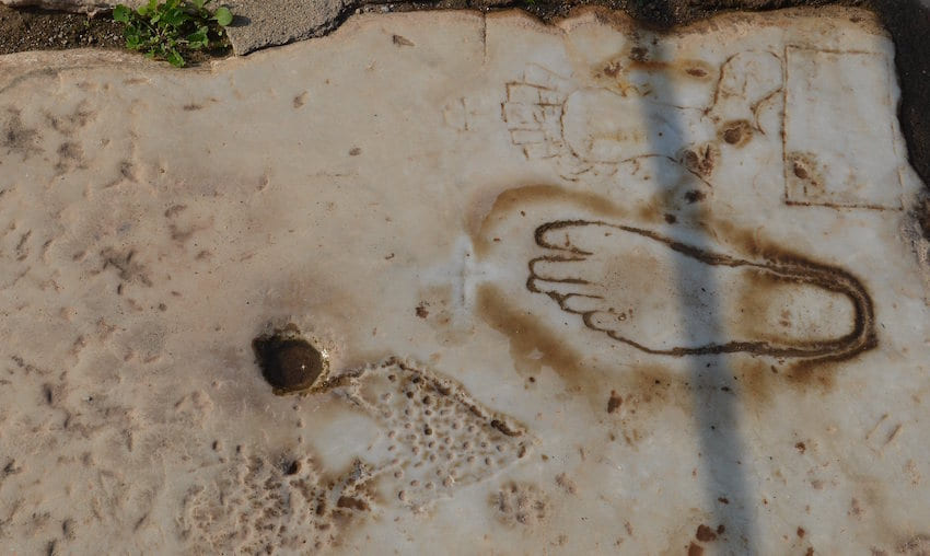 Grabados antiguos en una losa de mármol de Éfeso: la silueta de un pie, una figura femenina y un panel rectangular de líneas